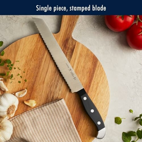 Serrated bread knife on a wooden cutting board with garlic, tomatoes, and a cloth.